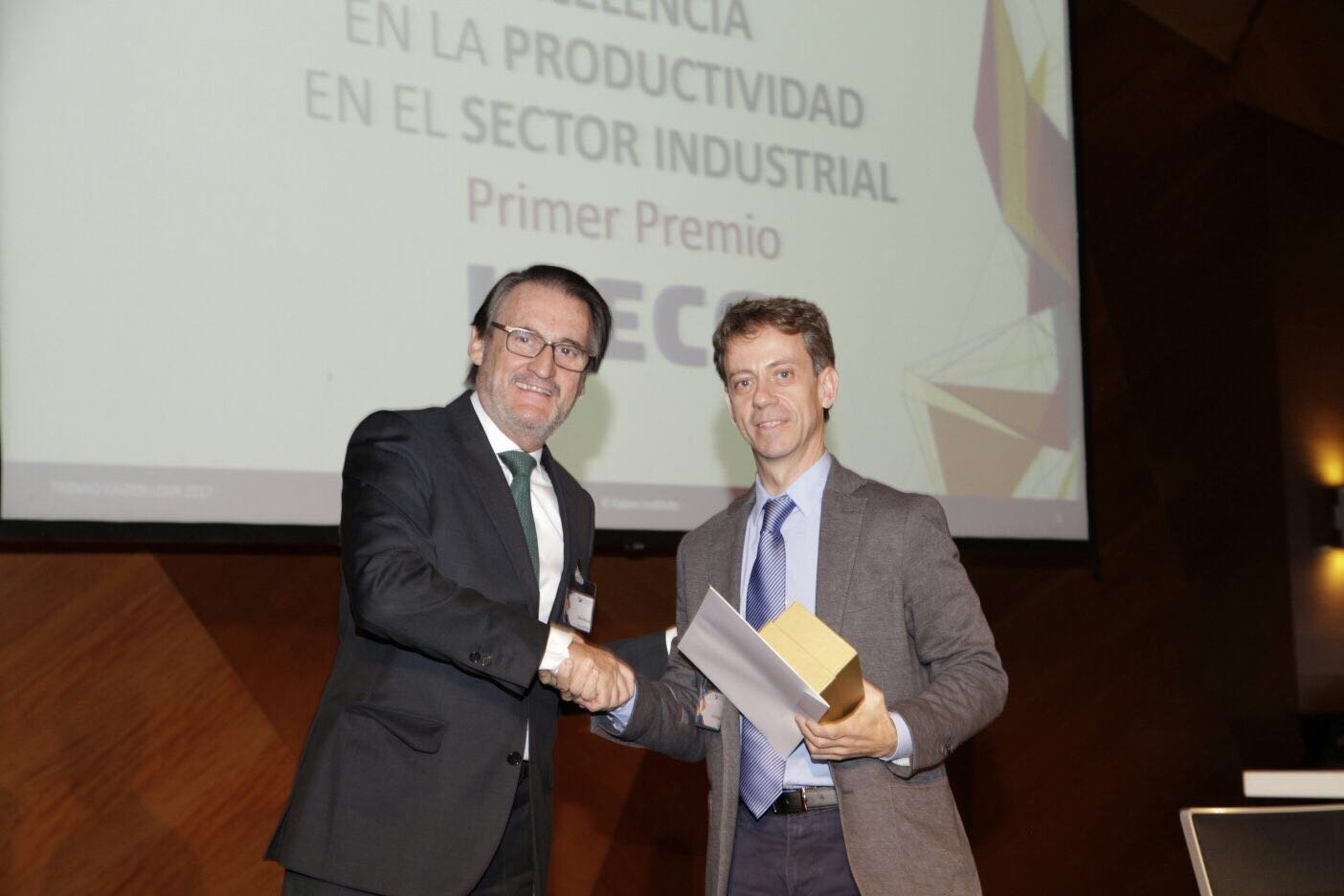 Jaime Revilla estrechando la mano a otro hombre que sostiene un premio