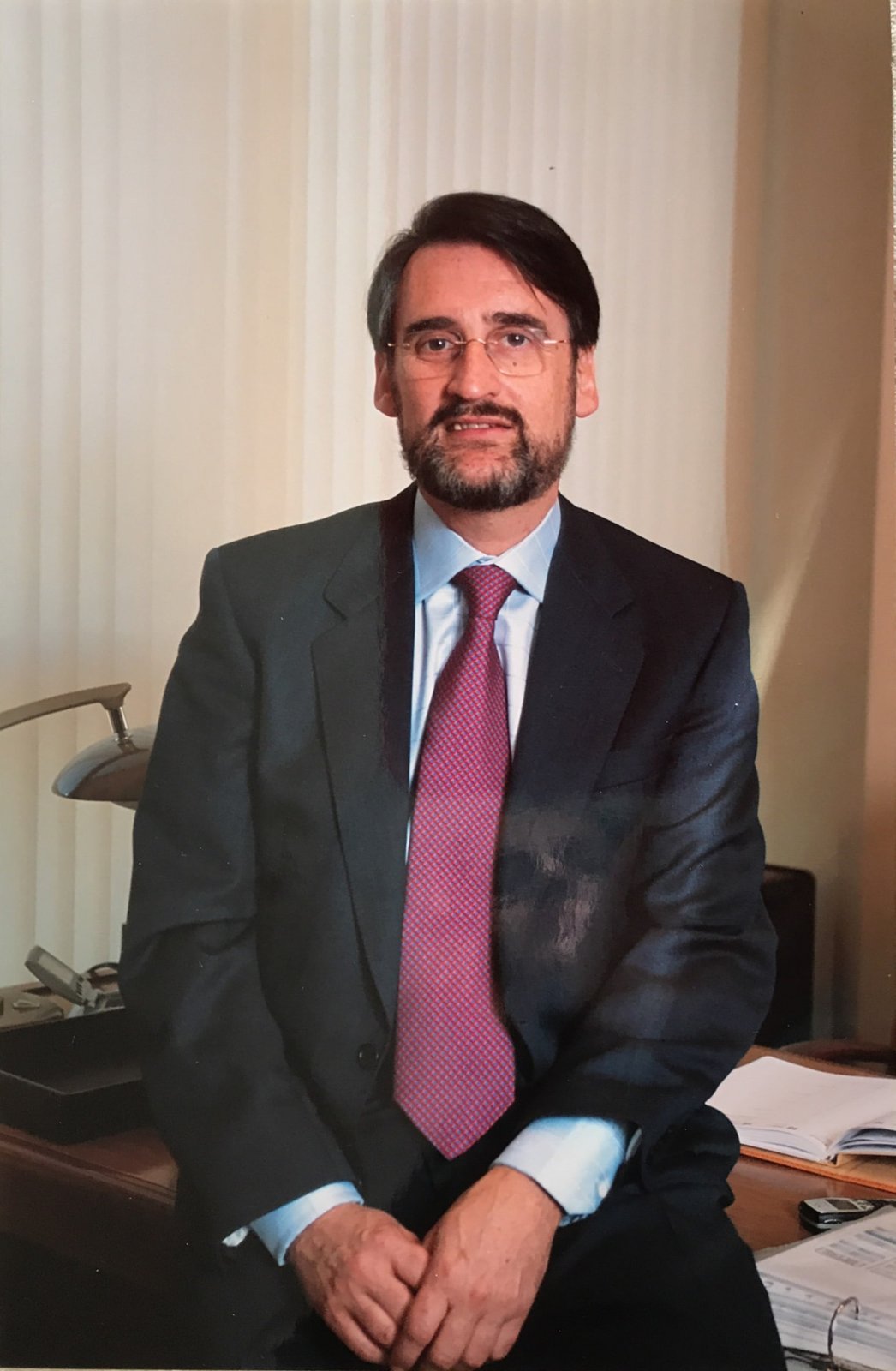 Jaime Revilla sentado en el borde de su mesa de despacho, con corbata granate