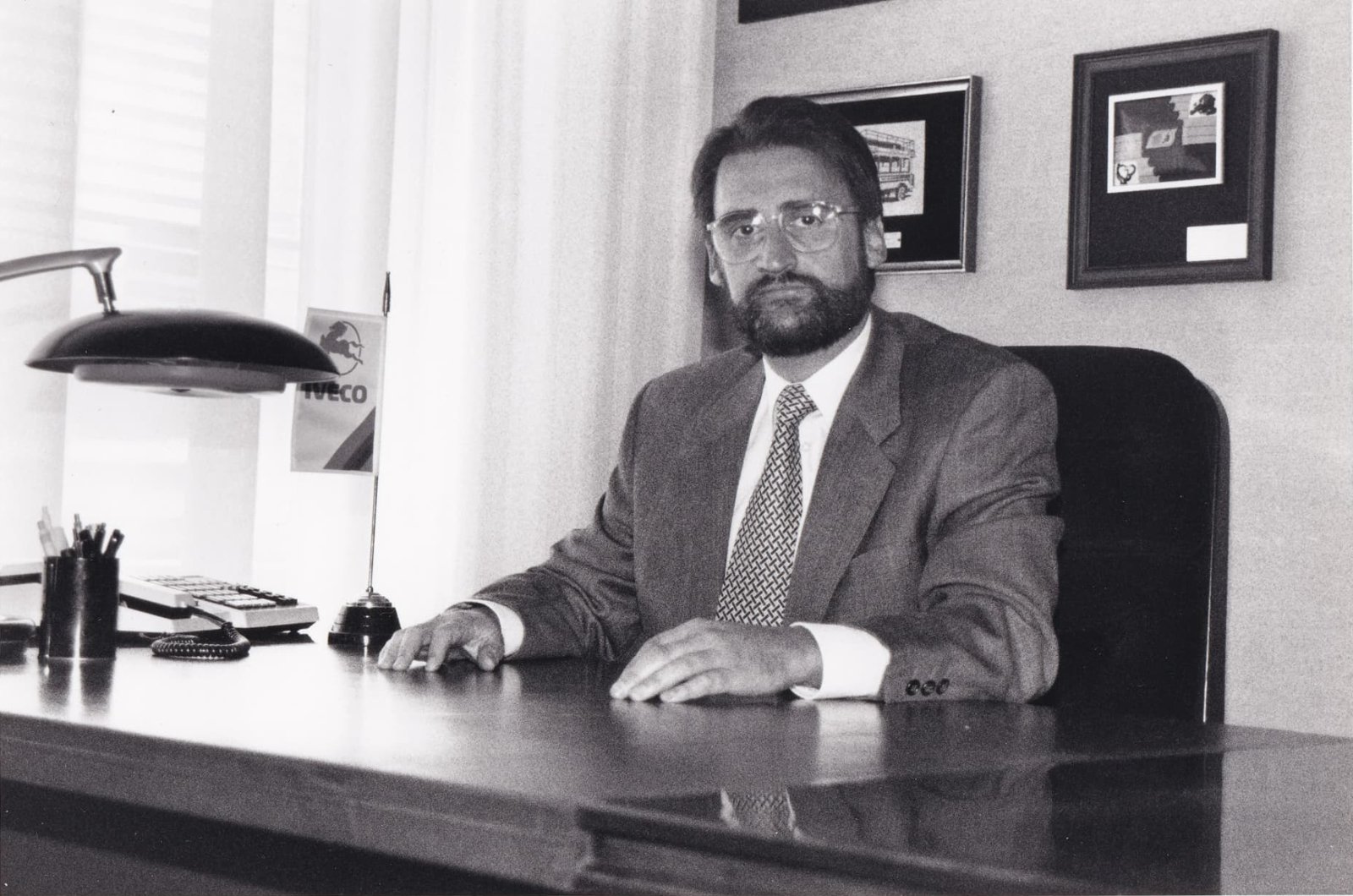 Fotografía en blanco y negro de Jaime Revilla sentado en su mesa, con un banderín de Iveco